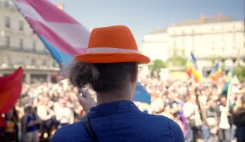 pride d'Angers, avec en premier plan, Syntia, femme trans, de dos, avec un chapeau orange CFDT, et un drapeau lgbt